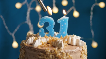 Birthday cake with 31 number candle on blue backgraund set on fire by lighter. Close-up