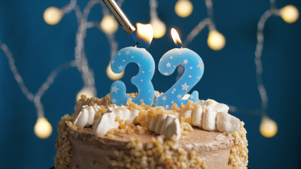 Birthday cake with 32 number candle on blue backgraund set on fire by lighter. Close-up