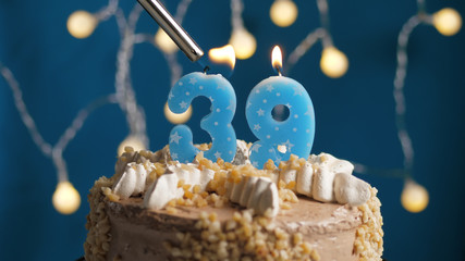 Birthday cake with 39 number candle on blue backgraund set on fire by lighter. Close-up