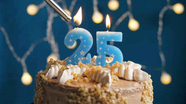 Birthday cake with 25 number candle on blue backgraund set on fire by lighter. Close-up