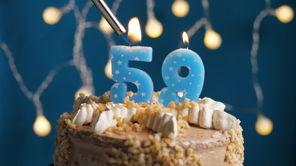 Birthday cake with 59 number candle on blue backgraund set on fire by lighter. Close-up