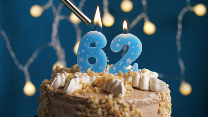 Birthday cake with 62 number candle on blue backgraund set on fire by lighter. Close-up