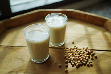 Soy milk homemade in glass cup decorated by soybean on wooden table background.