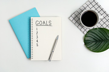 List of Goals. Creative flat lay of workspace desk with notebook planner, pen, plant and coffee on white background. Business, goals and planning concept. 