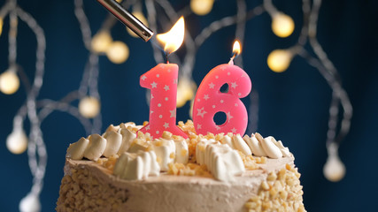 Birthday cake with 16 number candle on blue backgraund set on fire by lighter. Close-up view