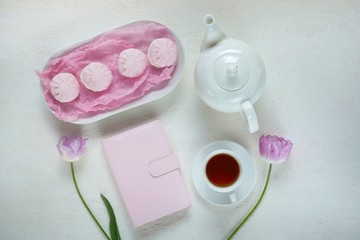 Obraz na płótnie Canvas Spring Flat lay.White cup with tea, pink diary,lilac tulips, pink marshmallows and a white teapot on a light background.top view, copy space.Spring season