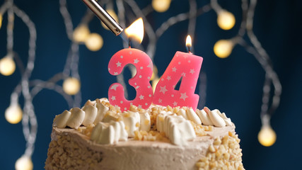Birthday cake with 34 number candle on blue backgraund set on fire by lighter. Close-up view