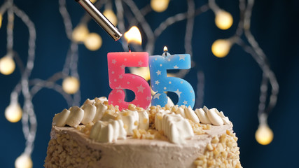 Birthday cake with 55 number candle on blue backgraund set on fire by lighter. Close-up view