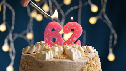 Birthday cake with 62 number candle on blue backgraund set on fire by lighter. Close-up view