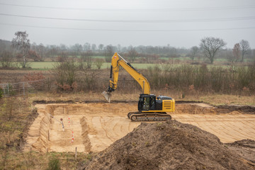 a building site there is a yellow excavator preparing the ground for foundations