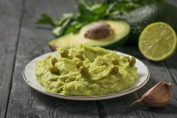 Green peas in a bowl of guacamole on a wooden table. Diet vegetarian Mexican food avocado.