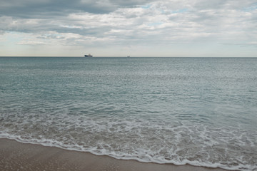 Fototapeta na wymiar Waves of the Mediterranean Sea on the beach in the afternoon. A dry cargo ship on the horizon.