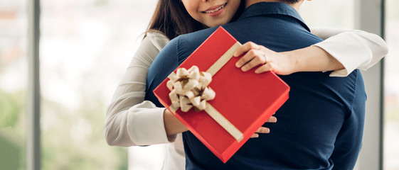 Young handsome man giving gift box surprise to girlfriend.Beautiful smiling woman hugging man at...