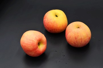 Three red apples on a black background indoors