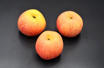 Three red apples on a black background indoors
