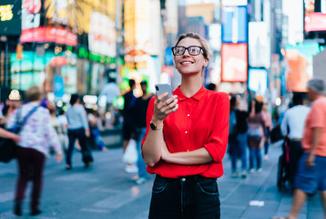 Caucasian female standing in crowded square with mobile phone in hands.Addicted to social network. Millennial technology user. Young woman browsing internet via app on smartphone. Tourist explore city