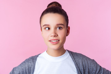 Portrait of adorable funny brunette teen girl with bun hairstyle in casual clothes fooling around with crossed eyes, having fun, childish positive face. indoor studio shot isolated on pink background