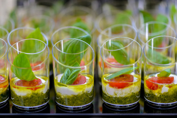 catering a lot of cheese snack with cherry tomato and a basil leaf in a small glass
