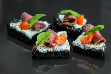 bruschettas on a black bun with meat from the chef on a black background