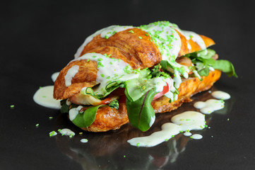 croissant stuffed with caesar salad on a black glossy background