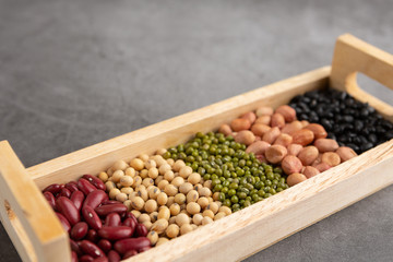 Red bean, black bean, green bean, soybean, peanut in the wooden tray placed on the black cement floor. High angle view.