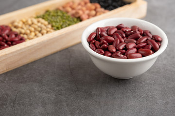 Red beans and grains in the white bowl and in the wooden tray placed on the black cement floor. High angle view.