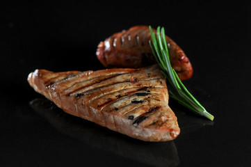 two grilled chicken fillets on a black background with a sprig of rosemary