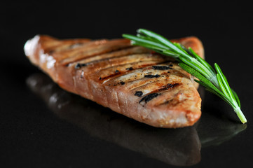 grilled chicken fillet on a black background with a sprig of rosemary