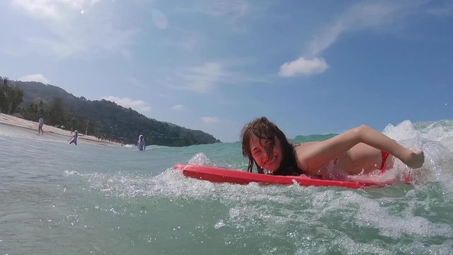 Young happy woman surfs the sea wave on bodyboard. Girl on holiday and vacation plays in the sea with surf board