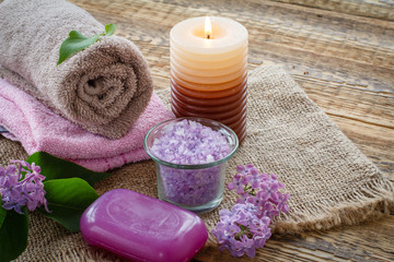 Obraz na płótnie Canvas Towels, soap, candle and lilac flowers on wooden background.