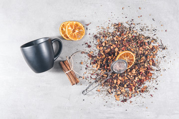 Fruit tea of dried flowers petals and berries with cinnamon, dry slice of orange and strainer - filter on gray table.