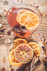 Glass cup of fruit tea with dry orange and cinnamon on wooden table.
