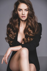 Portrait of a beautiful woman with a long hair in a black clothes. Young brunette woman in black sits on chair. Beautiful fashion model with brown hair, isolated on white background.