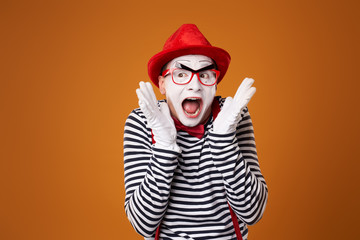 Fototapeta na wymiar Surprised young mime man in red hat and vest on orange background