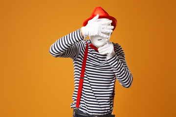 Fototapeta na wymiar Mime in red hat and in vest with white mask on orange background