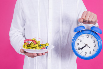 man holding plate with measuring tape and alarm clock, diet and health concept