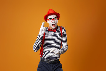 Surprised mime in white gloves and red hat looking at camera on orange background