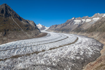 Stunning panorama view of the Great Aletsch Glacier from the hiking path above on a sunny summer day with blue sky and snow covered Swiss Alps in background, Canton of Valais, Switzerland