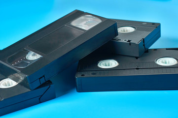 Heap of black old plastic vhs video cassettes lies on blue desk. Concept of 90s. Close-up