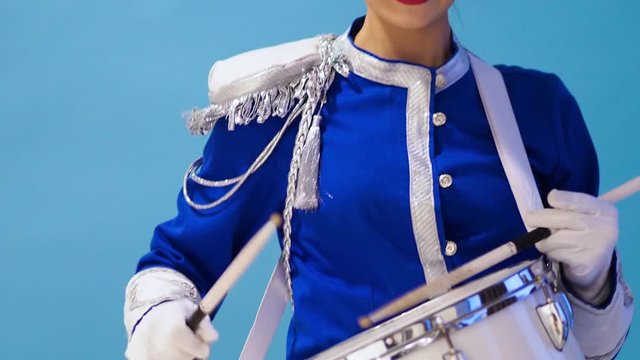 young female drummer in a bright blue uniform plays a drum roll. Blue background