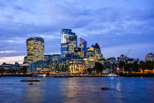 Blue night view of the illuminated skyscrapers in the City of London, a financial and business district in London, United Kingdom, with the River Thames from the South Bank