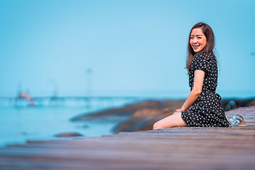 girl in black dress sitting by posing and relaxing on the walkway wood with smile happy in vacation trip and in sea view a happy holiday and happy time in vacation