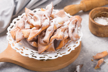 Italian Frappe or chiacchiere (hvorost) - typical Italian carnival fritters dusted with powdered sugar on concrete  table.