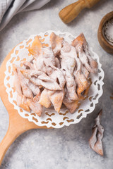 Italian Frappe or chiacchiere (hvorost) - typical Italian carnival fritters dusted with powdered sugar on concrete  table.