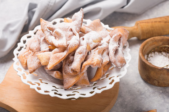 Italian Frappe or chiacchiere (hvorost) - typical Italian carnival fritters dusted with powdered sugar on concrete  table.