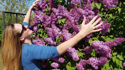 Woman in garden. Pretty woman is hugging by both hands huge luxuriant lilac bush with purple flowers. Smiling young woman with long hairs. Springtime outdoor sunny day. Happiness concept.