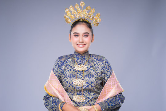 A beautiful Malaysian traditional female dancer with a charming smile performing a cultural dance steps in a traditional outfit. Half length isolated in grey.