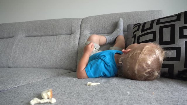Funny smiling boy lying on sofa and eating white bread. Smooth camera motion
