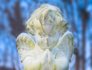 Beautiful little praying angel against blue sky. Ancient statue.