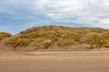 Looking back from the sea towards marram grass covered sand dunes and a lifebelt, at Formby in...